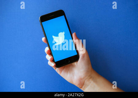 Kiew, Ukraine - Oktober 1, 2019: Studio geschossen von Hand mit Apple iPhone 8 mit Twitter Logo auf einem Bildschirm. Auf einem blauen Hintergrund. Stockfoto
