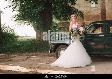 Glückliche Brautpaar steht neben einem stilvollen Auto während der Wanderung Stockfoto