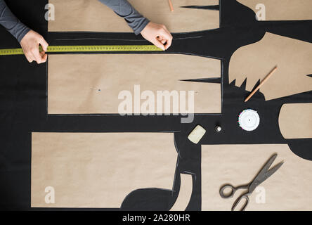 Der Schneider legt das Muster auf dem Stoff im Studio. Der Cutter umreißt das Muster am Arbeitsplatz. Stockfoto