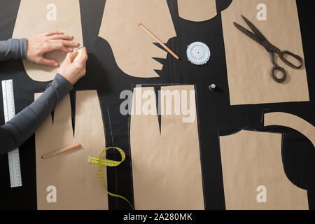 Der Schneider legt das Muster auf dem Stoff im Studio. Der Cutter umreißt das Muster am Arbeitsplatz. Stockfoto