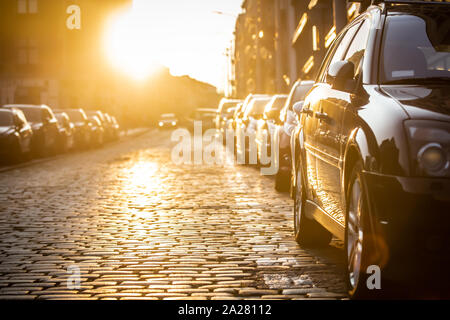 Autos auf der Seite der Straße geparkt, mit Sonnenuntergang im Hintergrund. Stockfoto