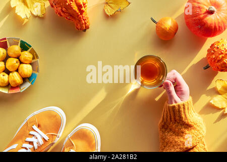 Gelbes Papier flach mit copy-Platz. Weibliche hand mit Tasse Tee, orange Kürbisse und Papier Platte mit Quitten. Stockfoto