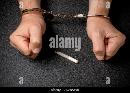 Mann die Hände in den Handschellen und eine Zigarette mit Marihuana auf schwarzem Hintergrund Stockfoto