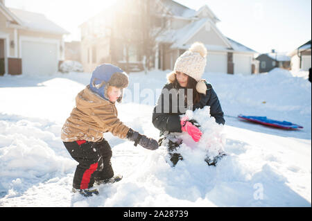 Bruder und Schwester spielen im Schnee Zusammen vor dem Haus Stockfoto