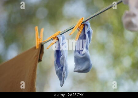 Blaue Socken sind auf einem Seil mit Wäscheklammern im Garten getrocknet Stockfoto