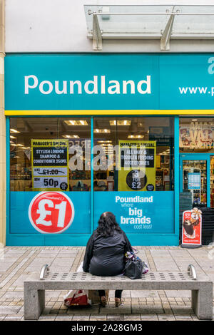 Eine Frau, die eine Pause vom Einkaufen vor Poundland shop in King's Lynn. Stockfoto