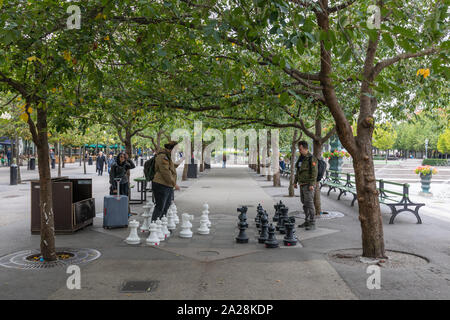 Stockholm, Schweden, September 2019: Zwei junge Männer spielen Schach im Freien mit großen schachfiguren unter einer Allee von Bäumen in Kungsträdgården. Stockfoto