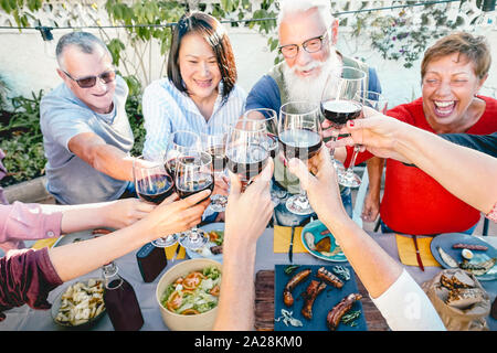 Gerne ältere Freunde Toasten mit Rotwein Gläser zum Abendessen im Freien - reife Menschen Spaß speisen zusammen außerhalb Stockfoto