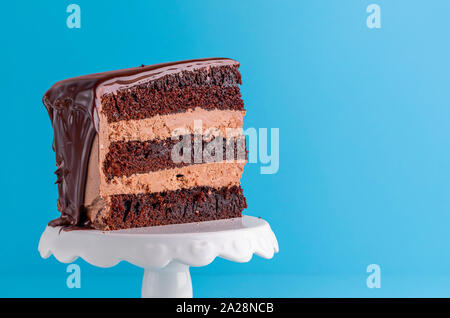 Appetitliche Stückchen Schokolade geschichteten Kuchen close-up auf blauem Hintergrund. Hausgemachte Kakao neue Jahr Stück Kuchen. Schokolade Zuckerguss Dessert. Stockfoto