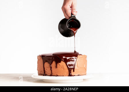 Verglasung Schokoladenkuchen mit geschmolzener Schokolade. Frau gießen Schokolade über Kuchen. Hausgemachte Kakao geschichteten Kuchen. Geburtstag Kuchen und Schokolade. Stockfoto