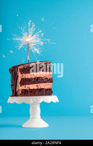 Geburtstag Konzept mit einem Stück Schokolade geschichteten Kuchen mit einer wunderkerze auf die Oberseite, auf einer blauen Tabelle. Neues Jahr Rahmen mit Stück Kuchen mit einem Feuerwerk. Stockfoto