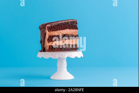 Nur ein Stück Schokolade Kuchen mit Kakao Glasur, auf Weißem und Blauem Hintergrund. Minimale Stück Kuchen. Festliche Layer Cake Slice Stockfoto