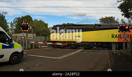 Eine schwarz-gelbe Diesellok kreuze Holywell bahnübergang als Polizei van wartet es auf der Nebenbahn nach lynemouth Power Station zu übergeben. Stockfoto