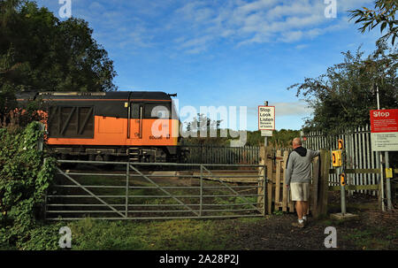 Eine orange Diesellok kreuze Stuten schließen Bahnübergang als Walker wartet, bis es an der Bahnstrecke Nebenbahn nach lynemouth Power Station zu übergeben. Stockfoto