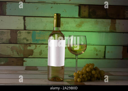 Flasche Weißwein mit einem Glas auf die Seite und seine Weintraube mit einem Hintergrund in grün beleuchtet serviert. Stockfoto