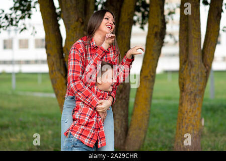 Mom, fröhlich lachend umarmt ihren Sohn, der Kniff und hob die Hände auf. Stockfoto