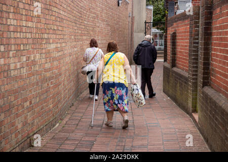 Eine behinderte Frau mittleren Alters hinunter die Straße mit krücken als Gehhilfe oder die Gehhilfe Stockfoto