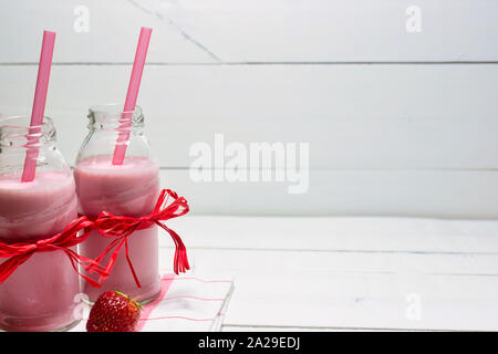 Erdbeer Joghurt in Flaschen und frische organische Erdbeere auf einem weißen Holztisch. Gesunde Ernährung Konzept. Stockfoto