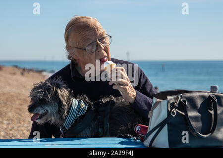 Ein älterer Mann, der mit seinem Hund am Meer ein Eis lecken Stockfoto