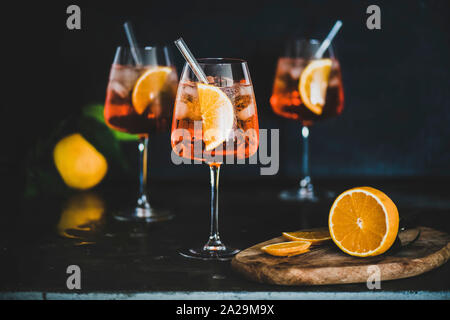 Aperol Spritz Aperitif mit Orangen und Eis im Glas mit umweltfreundlichen Glas Stroh auf konkrete Tabelle, schwarzer Hintergrund, selektiven Fokus. Sommer refres Stockfoto