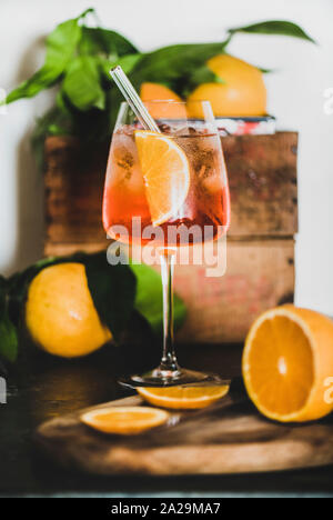 Aperol Spritz Aperitif mit Orangen und Eiswürfel im Glas mit umweltfreundlichen Glas Stroh auf konkrete Tabelle, weiße Wand im Hintergrund, selektiver Fokus, Stockfoto