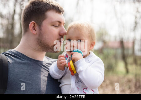 Junger Vater seine Tochter Holding bei einem Spaziergang in einem Park im frühen Frühling. Stockfoto