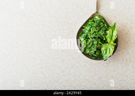 Hausgemachte Pesto in einem Löffel mit Basilikum auf einem weißen Tisch in der Küche. Ansicht von oben mit der Kopie. Pesto - Traditionelle italienische Soße für Fettuccine Stockfoto