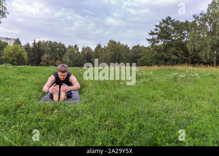 Man Yoga Asanas im City Park inspiriert. Fitness im Freien und Life Balance Konzept. Sitz nach vorne beugen Pose oder Paschimottanasana Stockfoto