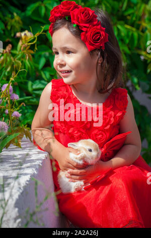 Ein wunderschönes kleines Mädchen im roten Kleid Holding ein Kaninchen. Ein Kind mit einer henz. Kinder und Tiere. Stockfoto