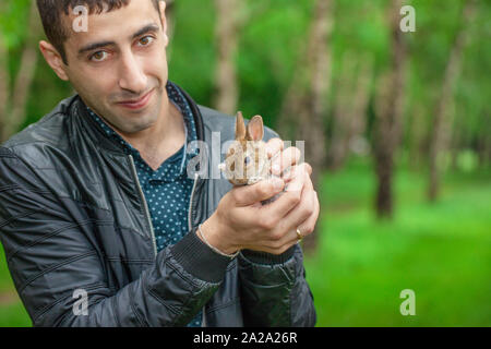 Porträt eines Mannes mit einem Kaninchen in seinen Händen. Der Kerl stellt mit einem Patz. Ein Mann hält einen flauschigen Nagetier. Stockfoto