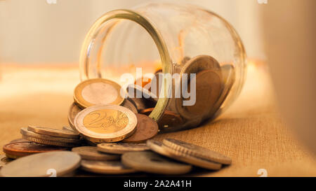 Münze jar umgeworfen auf dem Tisch mit Euro Münzen. Dieses Bild kann dazu verwendet werden, verschiedene Konzepte zu Geld zu vertreten. Stockfoto