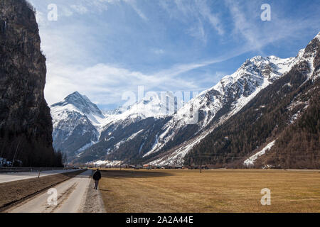 Frau entlang einer Straße im Ötztal auf einer klaren Frühlingstag, mit Schnee bedeckte Berge in der Ferne, in der Region Tirol in Österreich Stockfoto