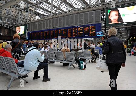 Passagiere warten auf Züge beobachten Sie die Abfahrt Board von Glasgow Central Station Stockfoto