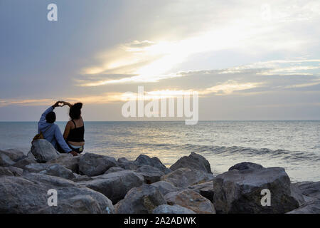 Colombia Riohacha Menschen schwimmen und entspannen am Strand. Das Sitzen auf den Felsen beobachten Sonnenuntergang. Die liebe Zeichen, ein Herz, das mit zwei Händen 26-6 - Stockfoto