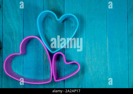 Farbige herzförmige Ausstechform Zahlen bilden eine dekorative Blüte, sitzen auf den blauen Hintergrund und Holz gesehen von oben Stockfoto