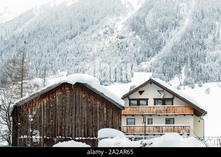 Österreichische Alpine Village malerische Landschaft mit kleinen Chalet und hölzernen Scheune, Kiefer Wald Bäume und die schneebedeckten Berge im Hintergrund. Kalten frostigen Stockfoto