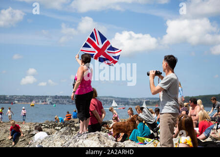 Eine Frau, die den britischen Union Jack Flagge und ein Mann mit einem Fernglas am Meer in St. Mawes, Cornwall, Großbritannien. Öffentliche sammeln am Strand beobachten die RNLI (Rettungsboote Nächstenliebe) von Schloss zu Schloss Schwimmen 2013. Diese Veranstaltung Geld Fundraising für die Rnli, am letzten Tag der Truro und Penwith College Fal River Festival dauert. Oder einfach nur ein symbolisches Bild Brexit zu illustrieren. Stockfoto