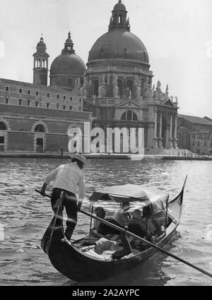 Ein gondoliere nimmt Touristen durch den Canal Grande. Am Ufer der Basilika di Santa Maria della Salute gesehen werden kann. Stockfoto