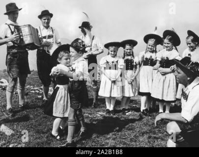 Zwei Kinder Tanz eine traditionelle bayerische Tanz, von Musikern und anderen Kindern umgeben. Undatiertes Foto, vermutlich aus den 60er Jahren. Stockfoto