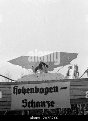 Das Bild zeigt die Hobby-Tüftler Hans Frank mit seiner Konstruktion, die sieht aus wie ein 'fliegenden Schlitten". Anscheinend wollte er seinen Bau am Hohenbogen Ski Jump in der Nähe von Neukirchen zu versuchen. Die Schanze wurde 1952 gebaut, aber ab 1959 keine regelmäßigen Wettbewerbe dort gehalten wurden, und die Schanze wurde in den 1960er Jahren abgerissen. Stockfoto
