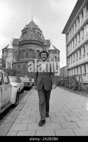 Das Bild zeigt die Pfarrer der St. Benno, Franz Xaver Eder, wandern auf einem Bürgersteig in der Klage. Im Hintergrund, die neo-romanischen katholischen Pfarrkirche St. Benno. Stockfoto