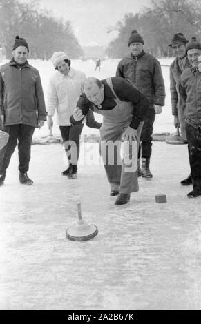 Dan Blocker, wer spielt die Rolle der Hoss Cartwright in der Fernsehserie Bonanzna, hier in der Mitte, mit einem Eis in der Hand beim Eisstockschiessen auf dem Nymphenburger Kanal. Hinter ihm sind einige Spieler. Stockfoto