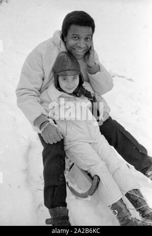 Roberto Blanco spielt im Schnee mit seiner Tochter Mercedes und einem Schlitten im Jahre 1970. Stockfoto