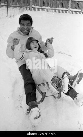 Roberto Blanco spielt im Schnee mit seiner Tochter Mercedes und einem Schlitten im Jahre 1970. Stockfoto