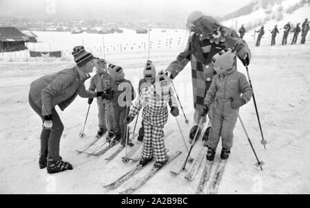 Kinder in den Skikurs in der Skischule Garmisch. Der Skilehrer ist ein Clown. Die Firma "Marker" wirbt für seine Sicherheit Skibindungen mit Banner. Stockfoto