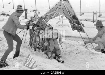 Kinder in den Skikurs in der Skischule Garmisch. Die Firma "Marker" wirbt für seine Sicherheit Skibindungen mit Banner. Stockfoto