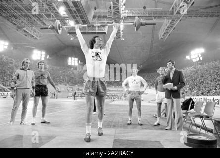 Fußballspieler Franz Beckenbauer (Mitte) plantscht im Gewichtheben am Sportpressefest in der Münchner Olympiahalle. Rechts im Bild, der Athlet und Moderator Erhard Keller. Stockfoto