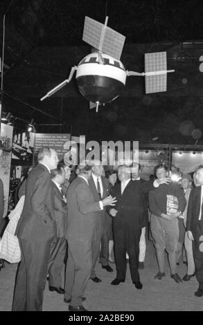 Der Ingenieur Wernher von Braun (4. von rechts, 1. Zeile) Besuche der Internationalen Transport Ausstellung (IVA) auf dem Messegelände Theresienhöhe in München. Über ihm ist ein Satellit. Stockfoto