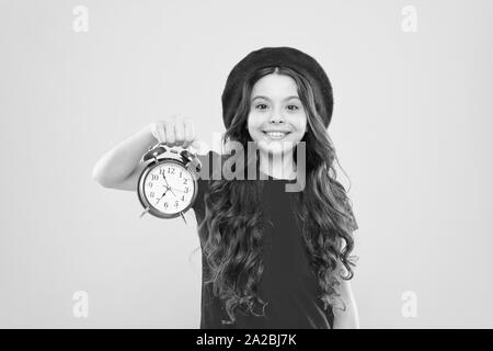 Shopping, Verkauf und Zeit Konzept. Pariser Kind auf Gelb. Kind mit Wecker. Zeitlose Mode. glückliches Mädchen mit langen Locken in Baskenmütze. Schönheit Friseur. Kleines Mädchen im französischen Stil hat. Stockfoto