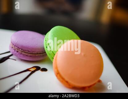 Orange, Grün und Violett macarons mit Schokoladensauce auf Weiß sqaure Platte Stockfoto